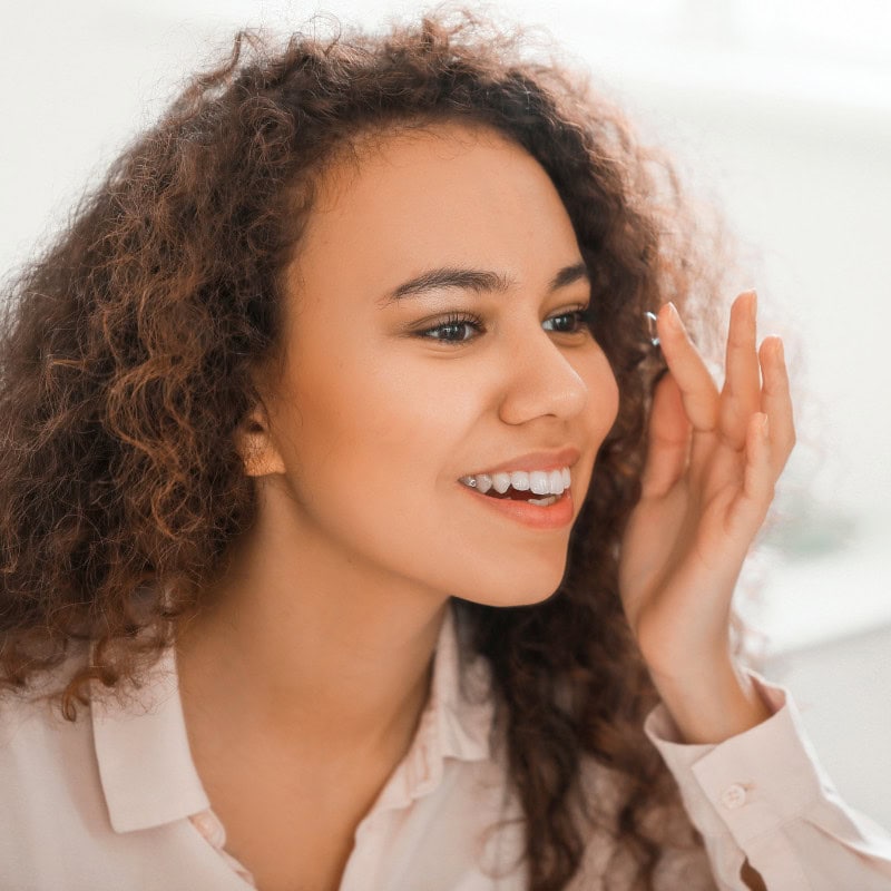 Woman putting contact lens into left eye.